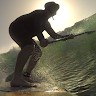 A silhouetted surfer rides a wave, positioned to catch the sunlight behind them, showcasing the dynamic motion of surfing in a coastal setting.